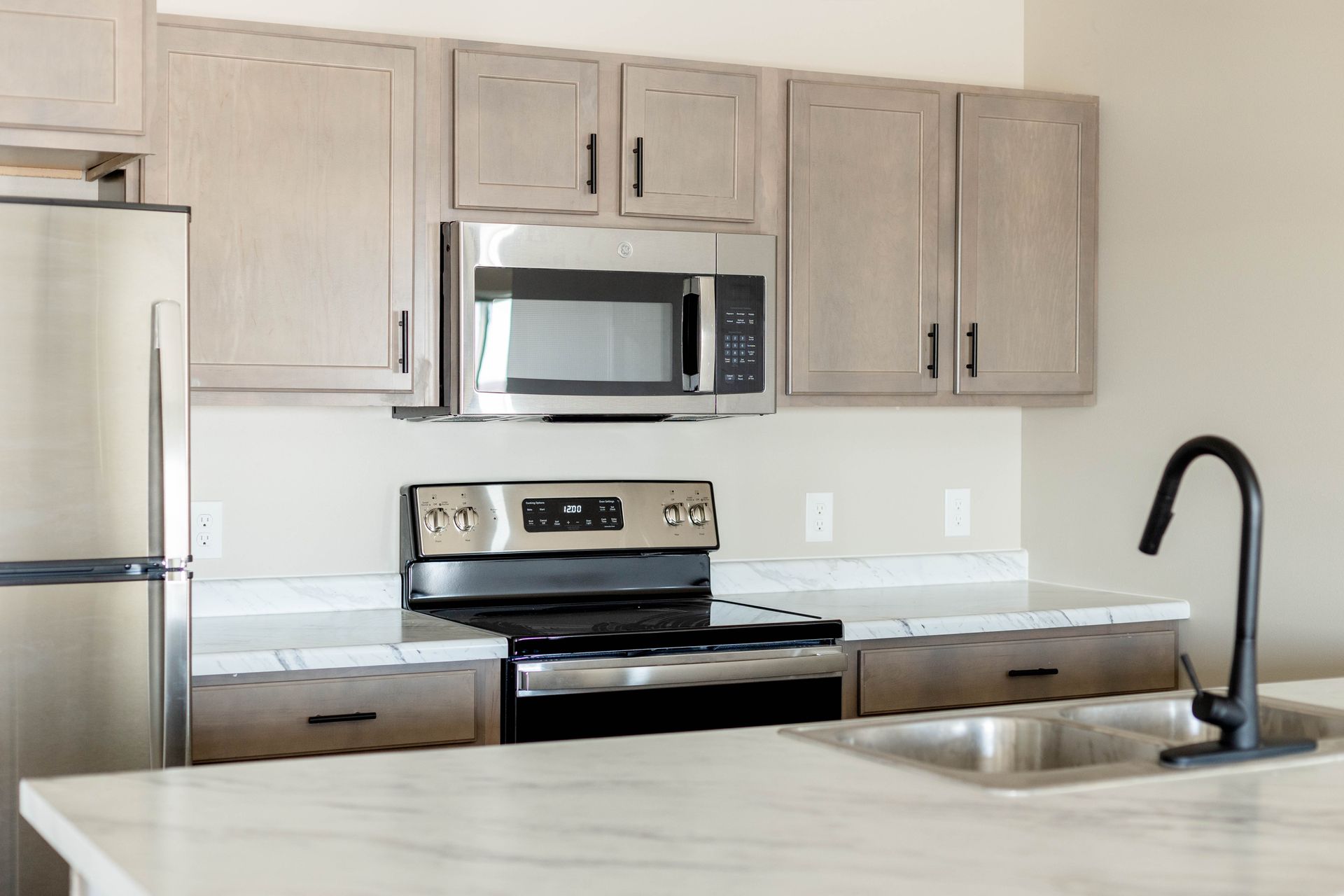A kitchen with a stove , microwave , refrigerator and sink.
