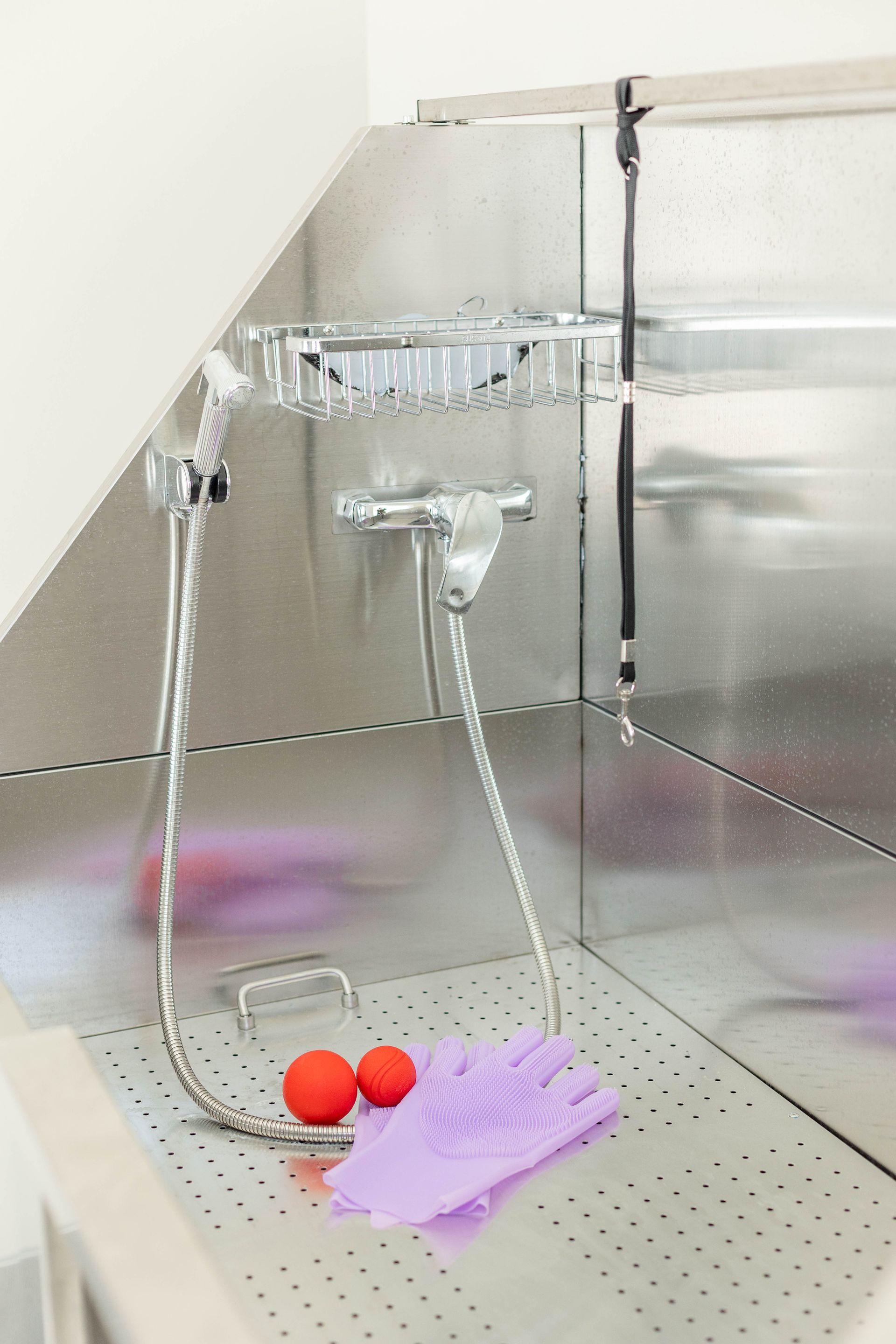 A stainless steel sink with a shower head and gloves on it.