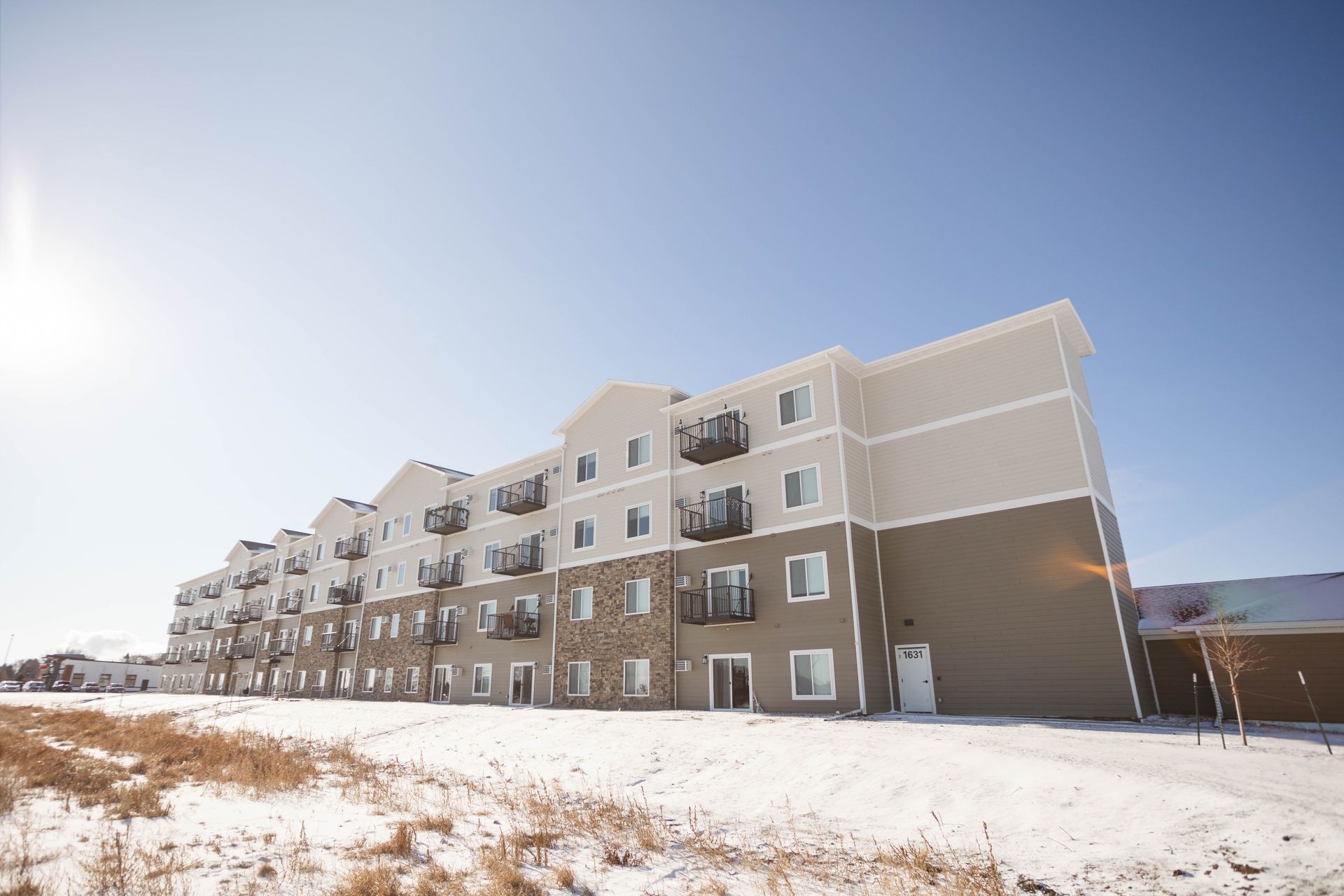A large apartment building with snow on the ground in front of it.