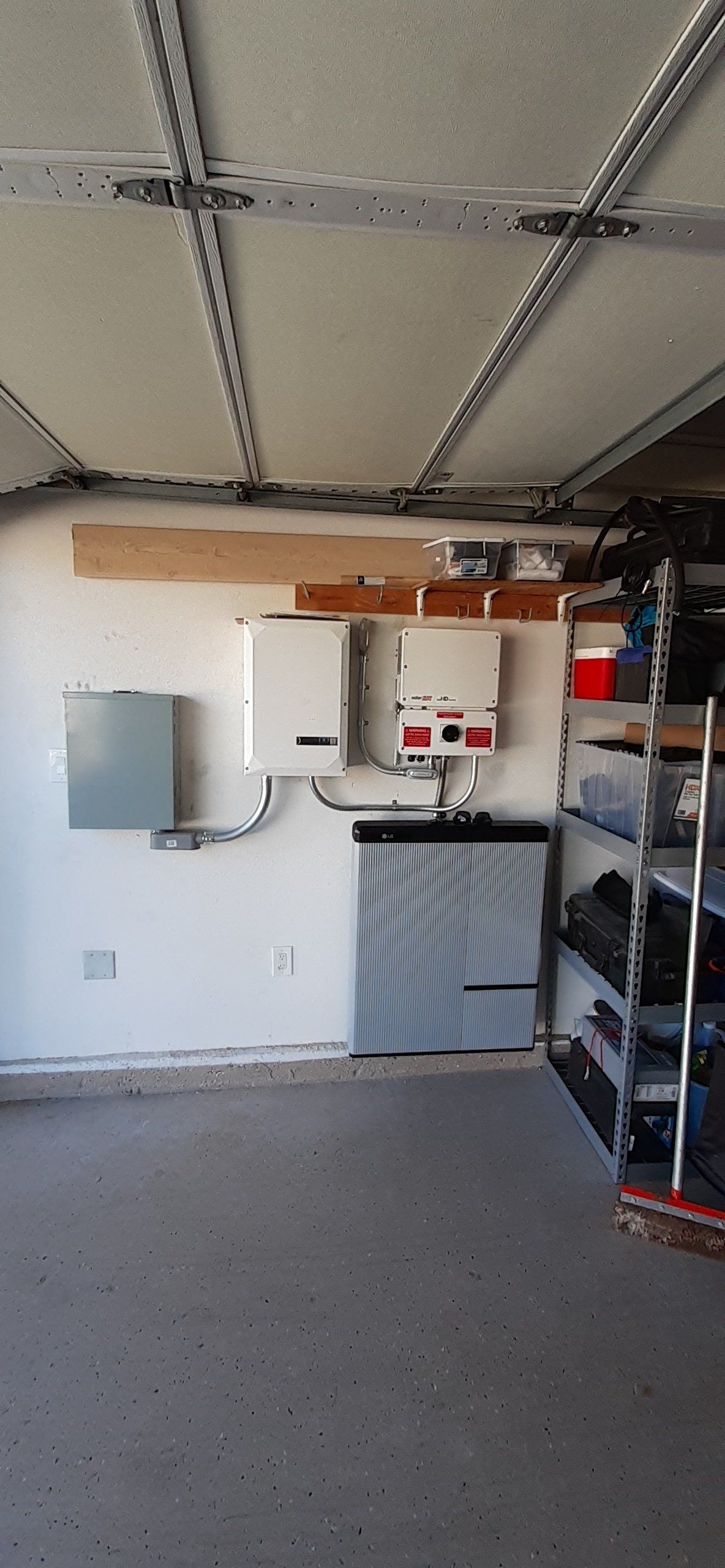 Garage interior with solar panel equipment on the wall, and storage shelves on the right.
