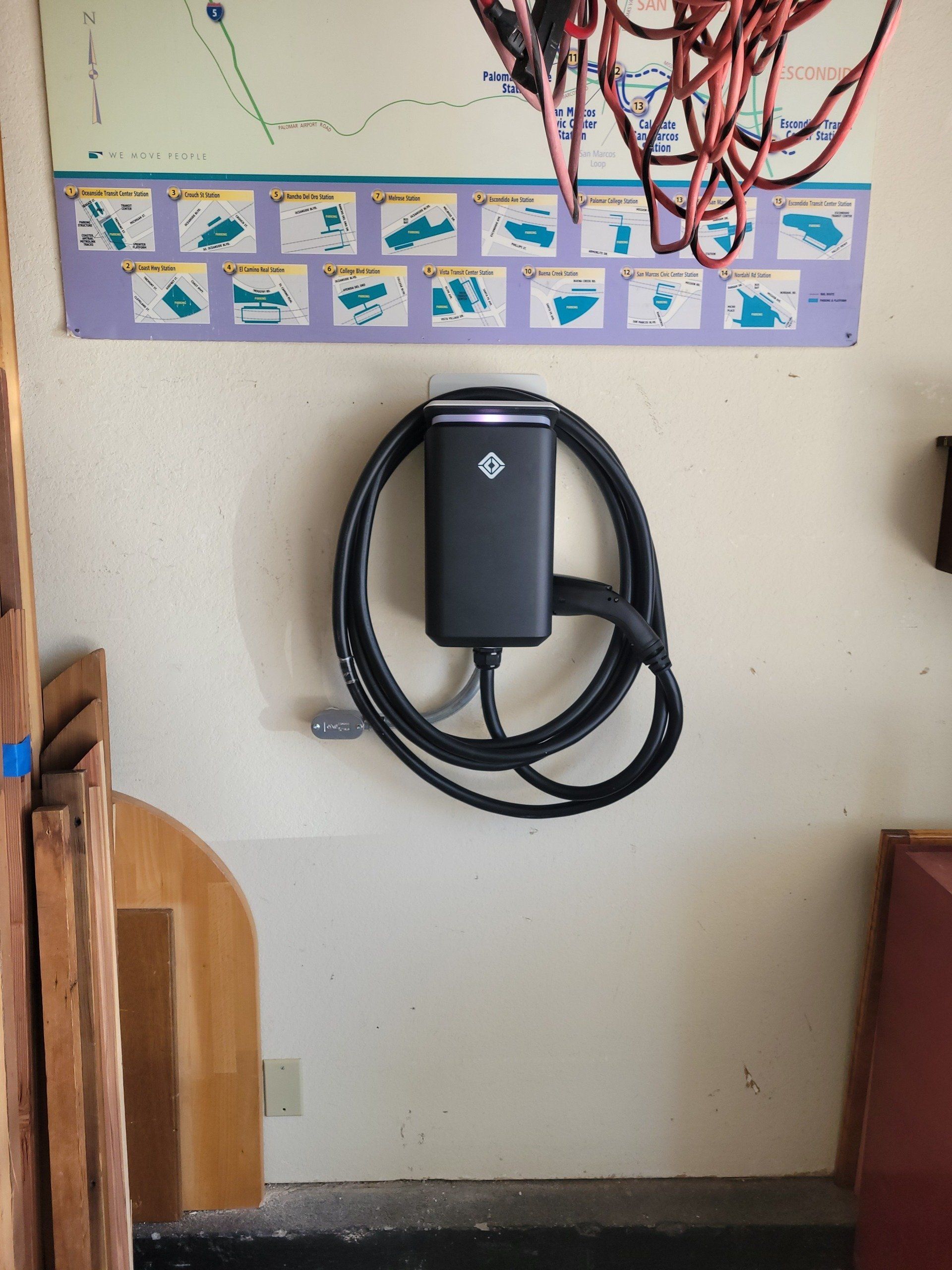 Black electric vehicle charger mounted on a cream wall. Map above, other objects on either side.
