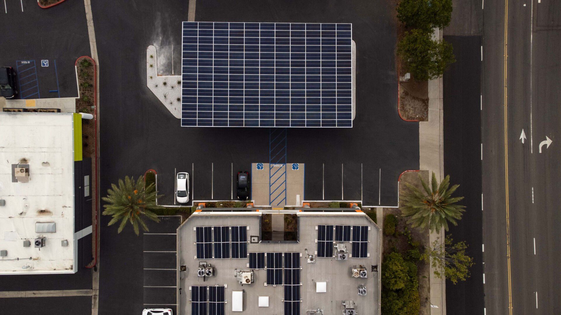 Aerial view: solar panels on building roof and canopy over parking lot.