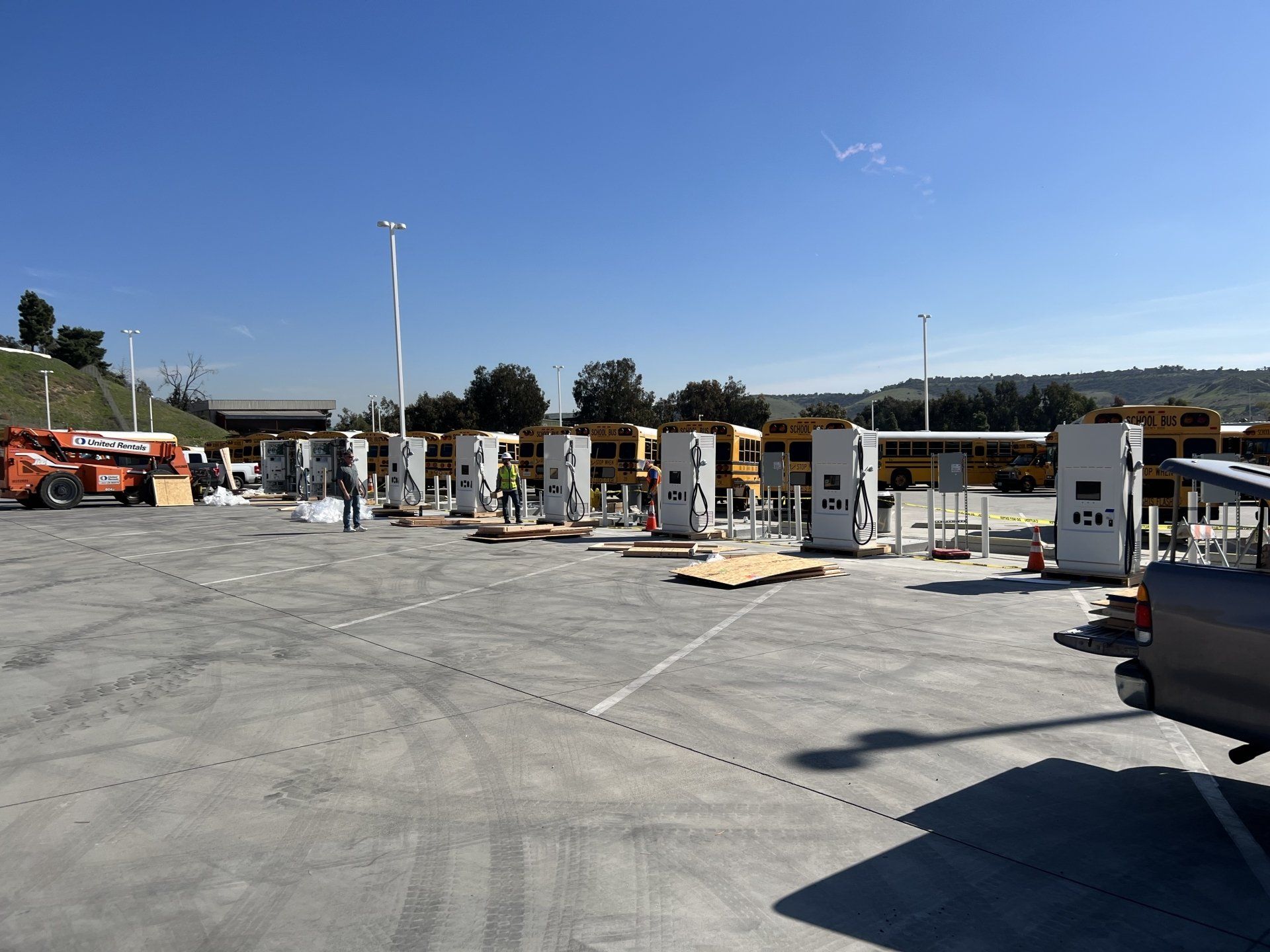 Electric vehicle charging station installation in progress, sunny day, school buses in background.