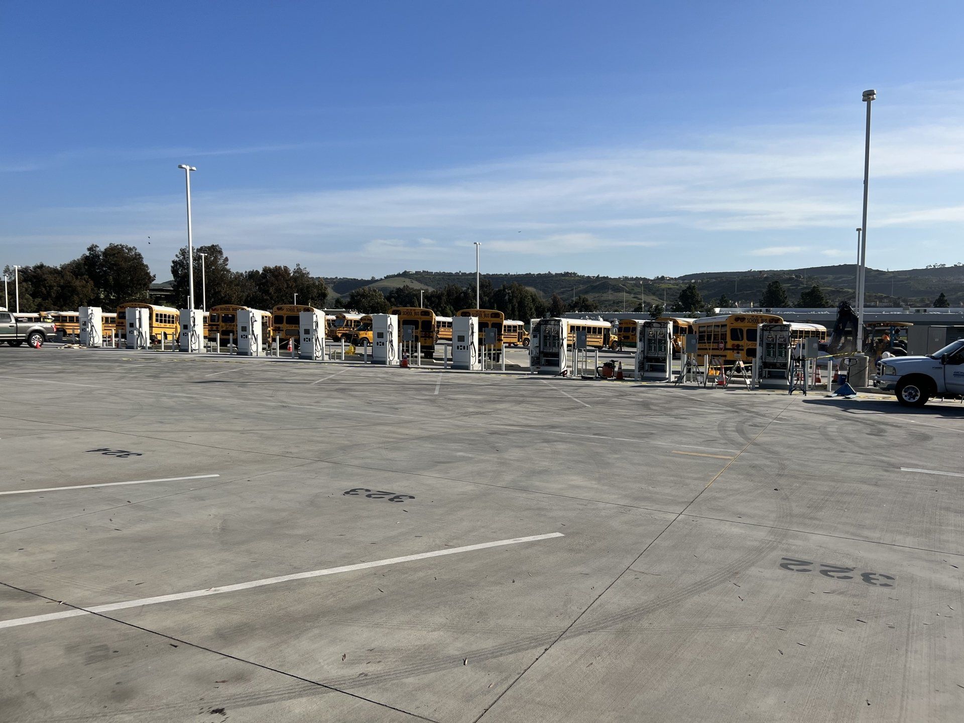 Empty toll booths at a toll plaza on a sunny day. Concrete ground, blue sky, and distant hills.