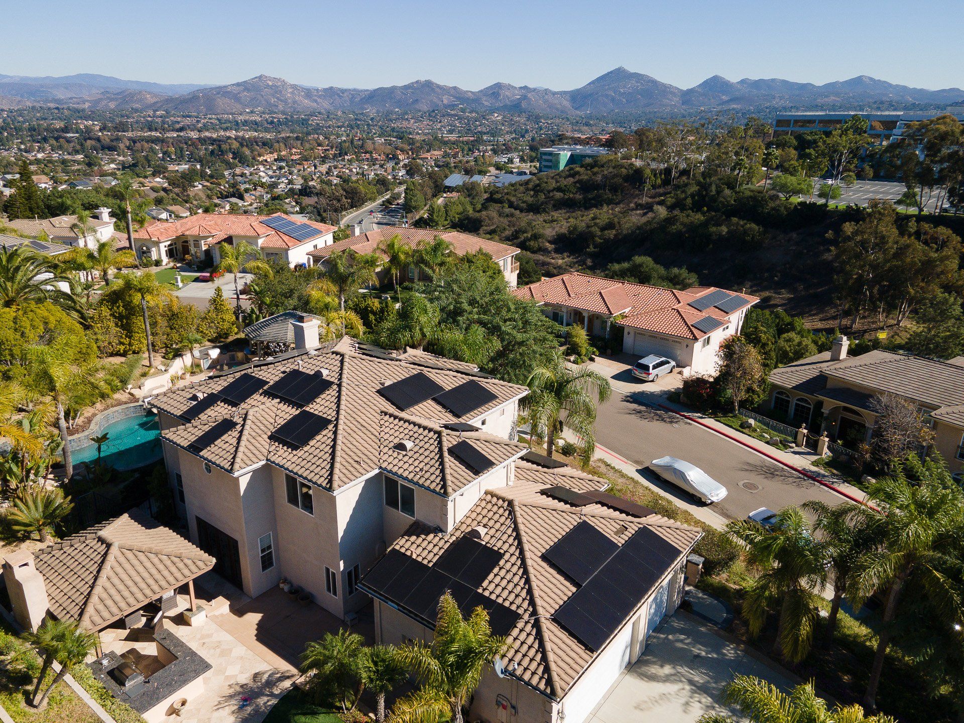 Aerial view of a suburban neighborhood with terracotta-roofed homes and mountains in the distance