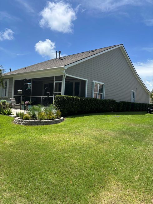 Single-story house with screened porch, white siding, and a large green lawn under a blue sky