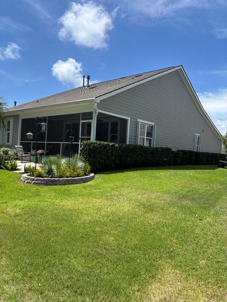 Single-story house with screened porch, white siding, and a large green lawn under a blue sky