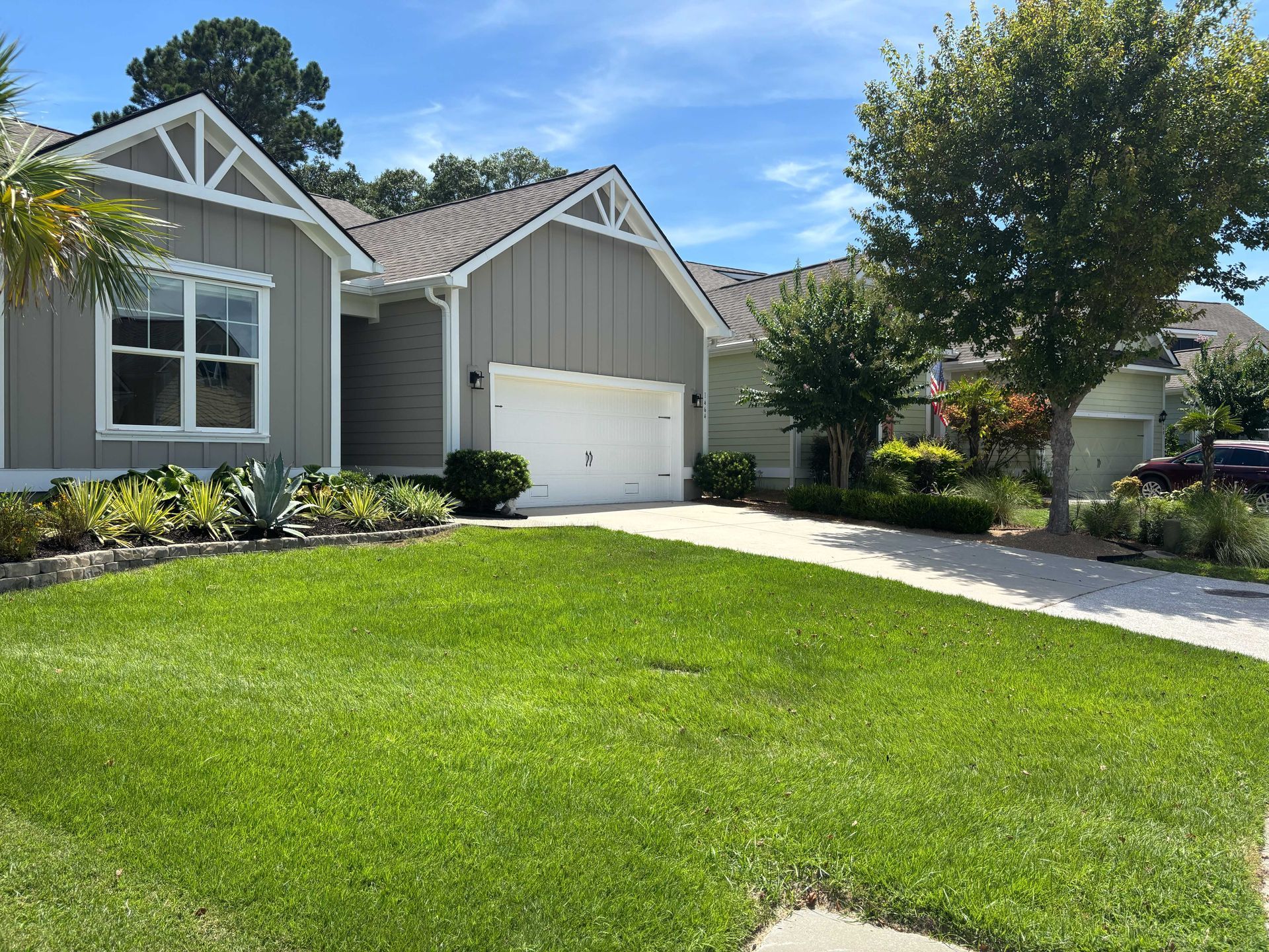 Suburban house with a green lawn, white garage, and driveway under a blue sky