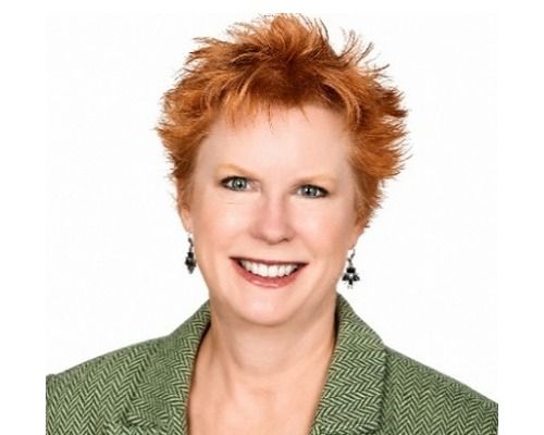 Smiling person with short red hair in a green blazer against a white background