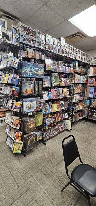 A board game store interior with shelves of games, a chair sits in the foreground.