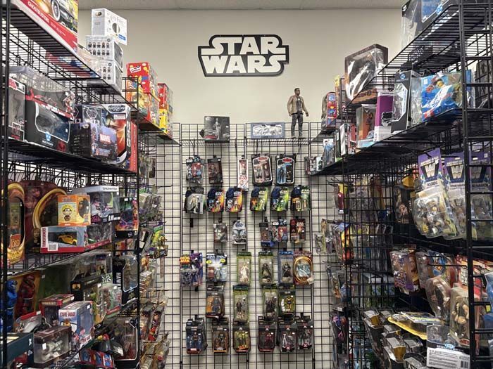 A toy store aisle with Star Wars merchandise displayed on shelves and a wall with a Star Wars logo.