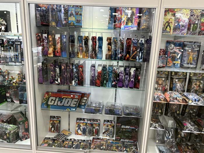A glass display case filled with action figures, including GI Joe, in a shop.