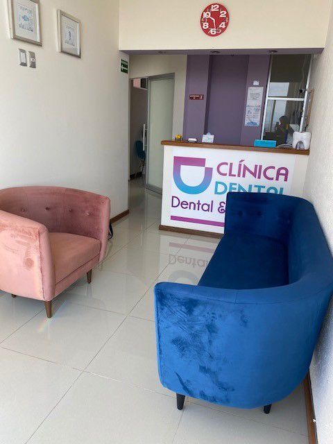 Sala de espera de la clínica dental con asientos de terciopelo azul y rosa. Mostrador de recepción al fondo.