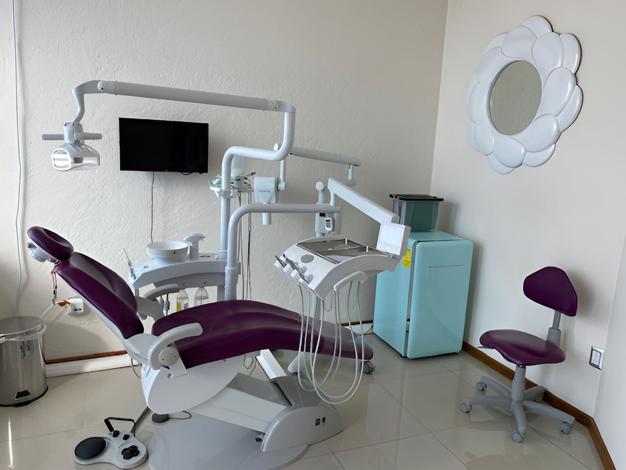 Consultorio dental con sillón y equipo de color morado y espejo decorativo.