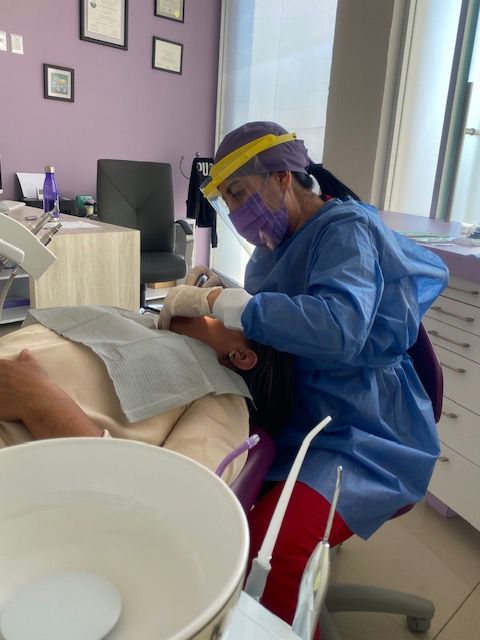 Dentista con equipo de protección trabajando con un paciente en un consultorio dental.