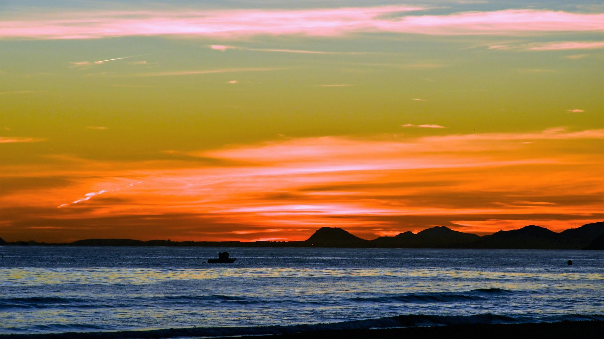 A sunset over a body of water with a boat in the distance.