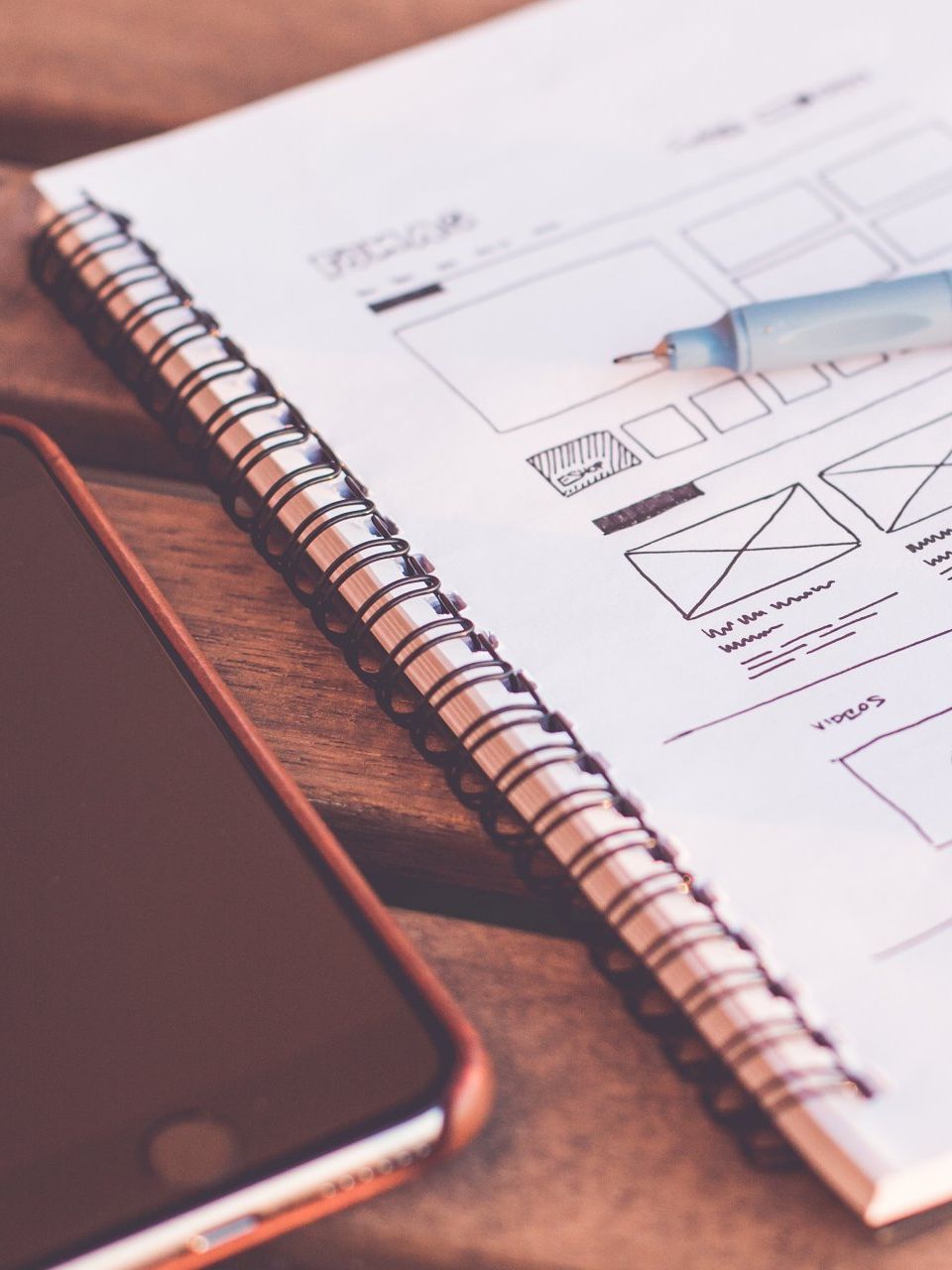 A cell phone is sitting next to a notebook with drawings on it
