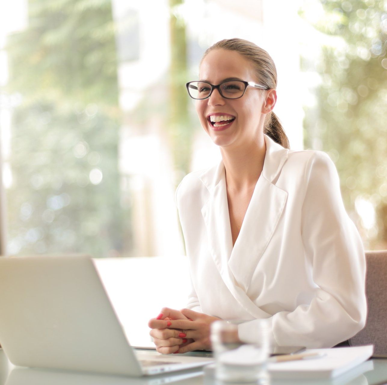 A woman wearing glasses is smiling while using a laptop