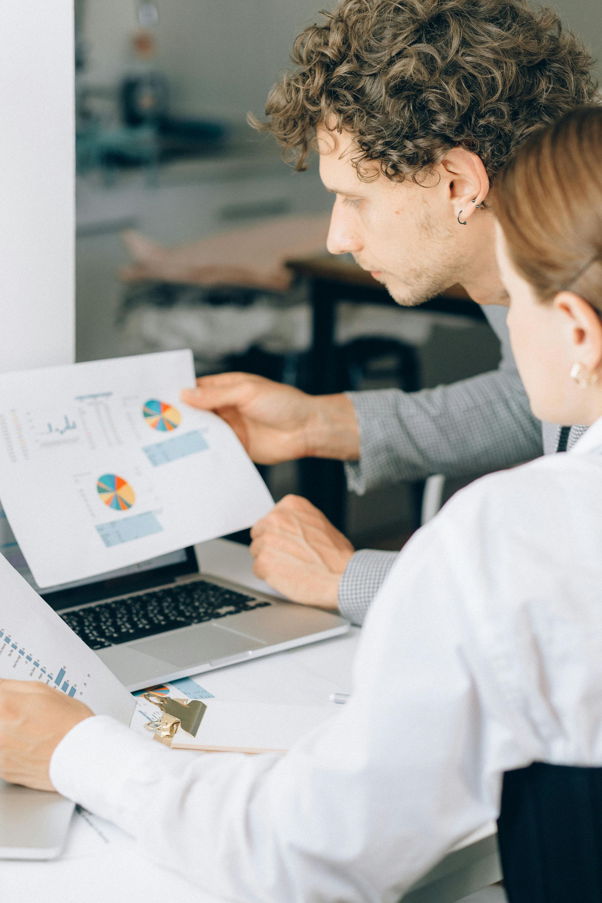 A man and a woman are looking at a piece of paper in front of a laptop.