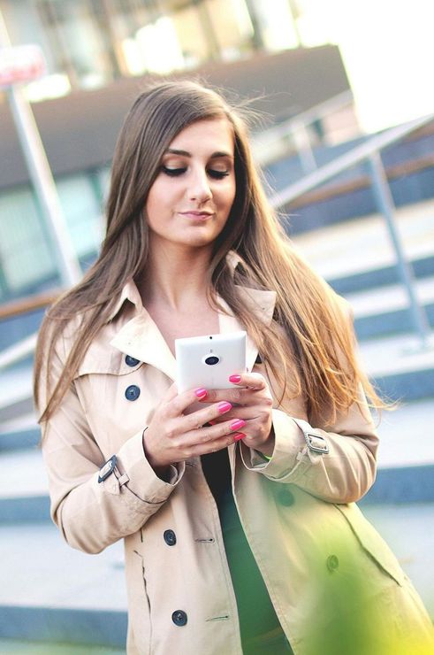 A woman in a trench coat is looking at her cell phone.