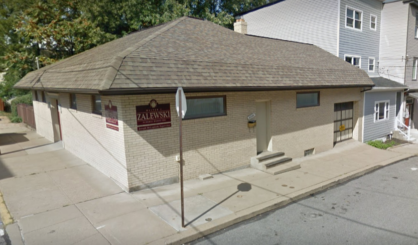 A corner view of a light-colored brick commercial building with a tan roof and a garage door on a street.