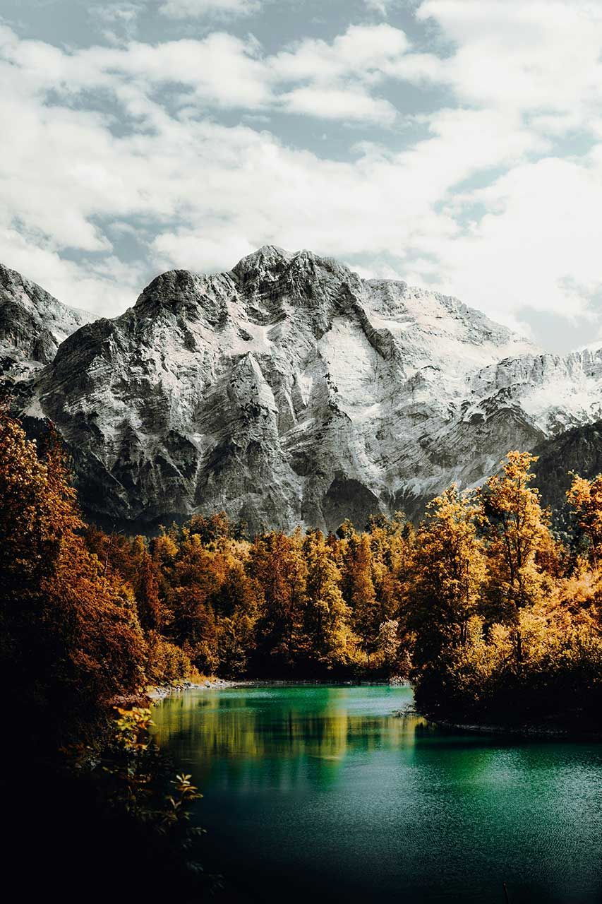 Snow-Capped Mountain Peaks Rising Above A Turquoise Lake Surrounded By Golden Autumn Trees Under A Cloudy Sky
