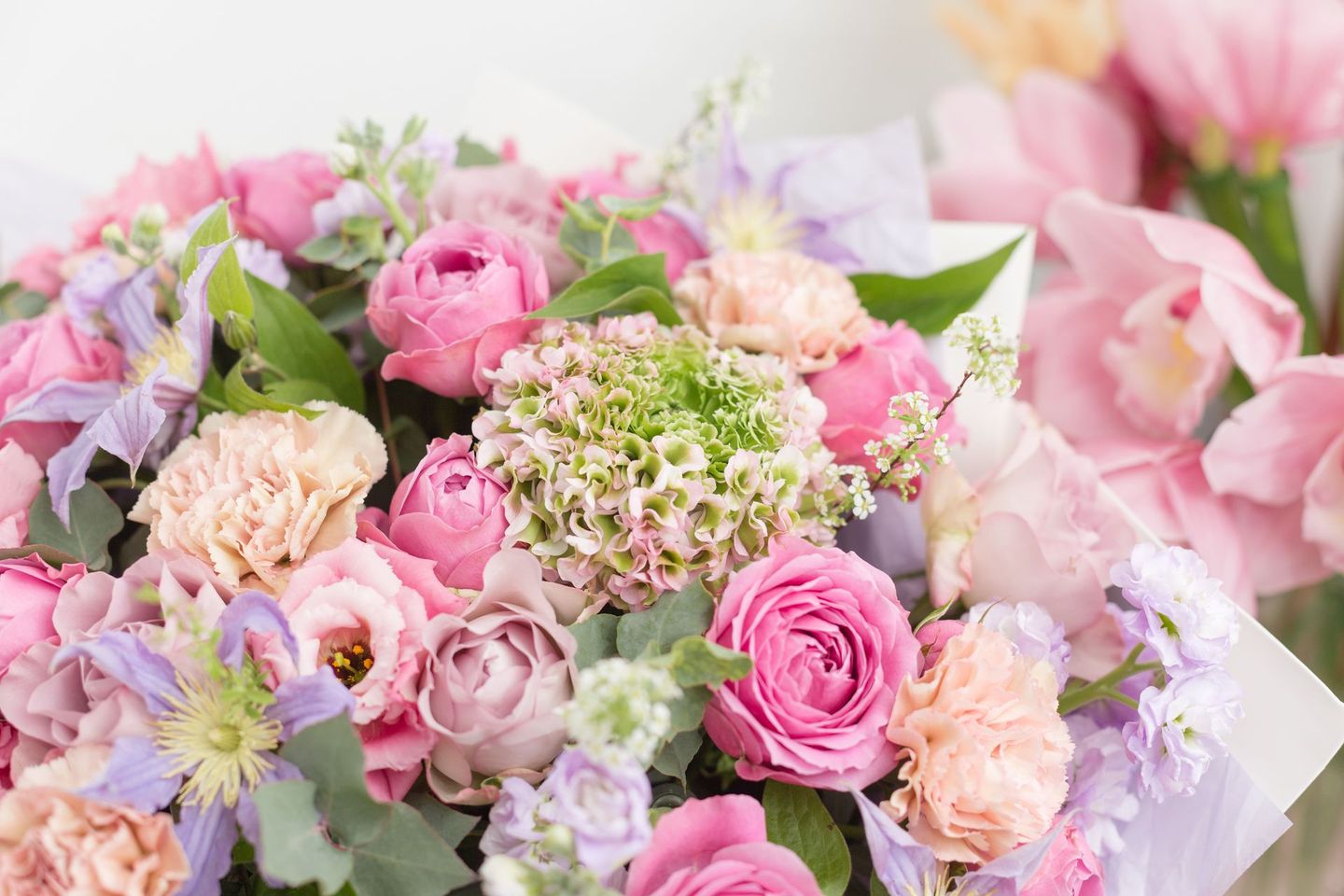 A dense, colorful bouquet featuring various shades of pink roses, light purple flowers, and green hydrangea blooms.