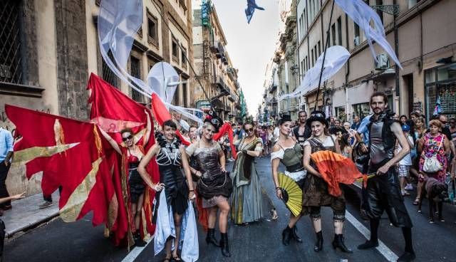 Un gruppo di persone cammina lungo una strada tenendo in mano delle bandiere.