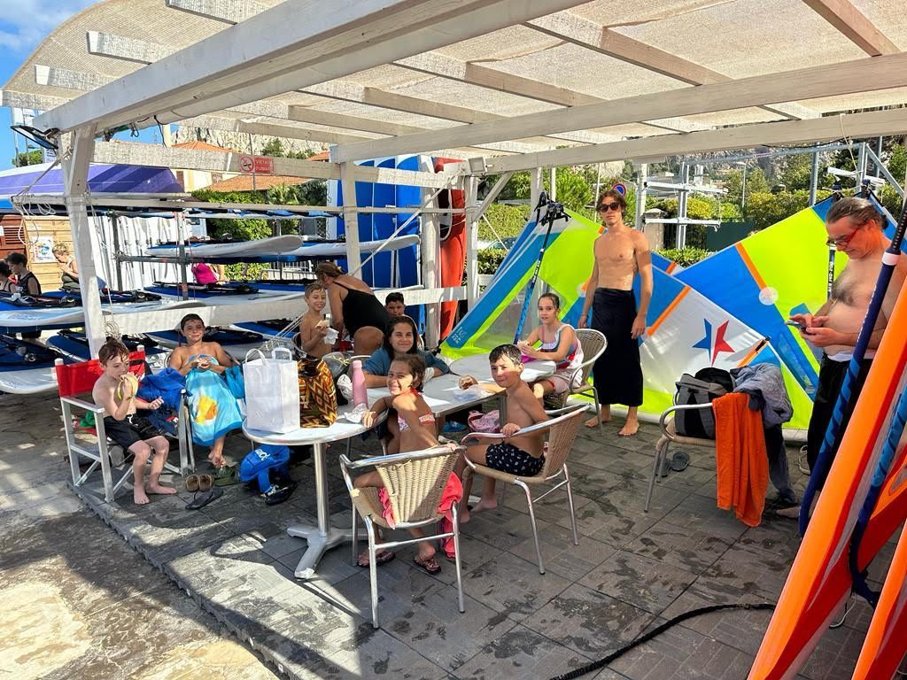 Un gruppo di persone è seduto a dei tavoli sotto una tettoia su una spiaggia.