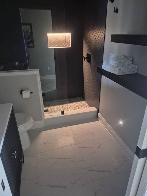 Modern bathroom with a walk-in shower, white tile floor, dark walls, and a lit mirror niche.