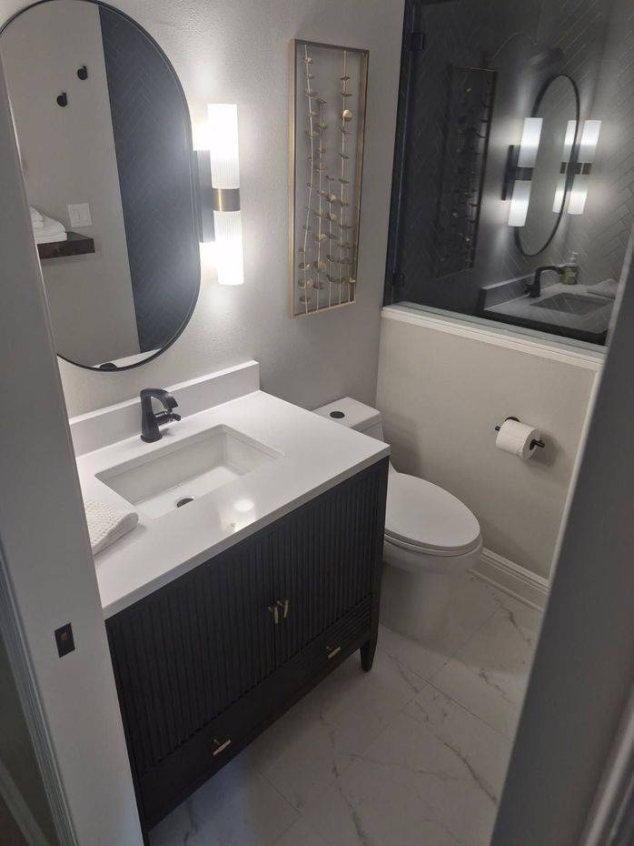 Modern bathroom with black vanity, oval mirror, toilet, and glass shower door