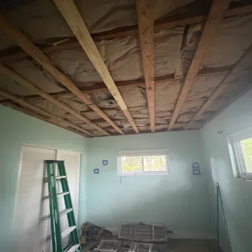 Room with exposed ceiling beams, mint-green walls, windows, and a green ladder during renovation