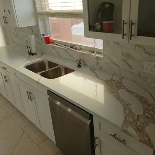 Modern kitchen with white cabinets, marble countertop, stainless sink, and built-in dishwasher by a window