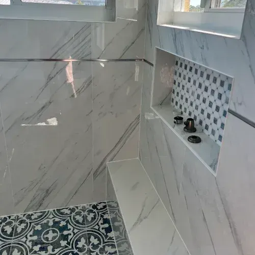 Modern tiled bathroom shower with recessed shelf, small mosaic accent, and patterned floor tiles