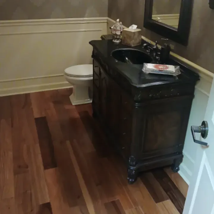 Small bathroom with dark wood vanity, sink, mirror, white toilet, and hardwood floor.