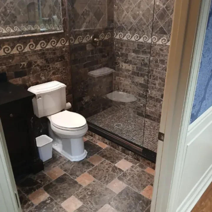 Small tiled bathroom with a toilet, shower stall, and dark vanity cabinet.