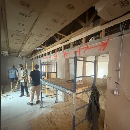Construction workers in a gutted hallway with scaffolding and exposed ceiling framing.