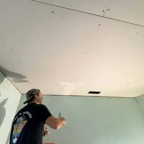 Person painting a light green wall and ceiling in a room under renovation