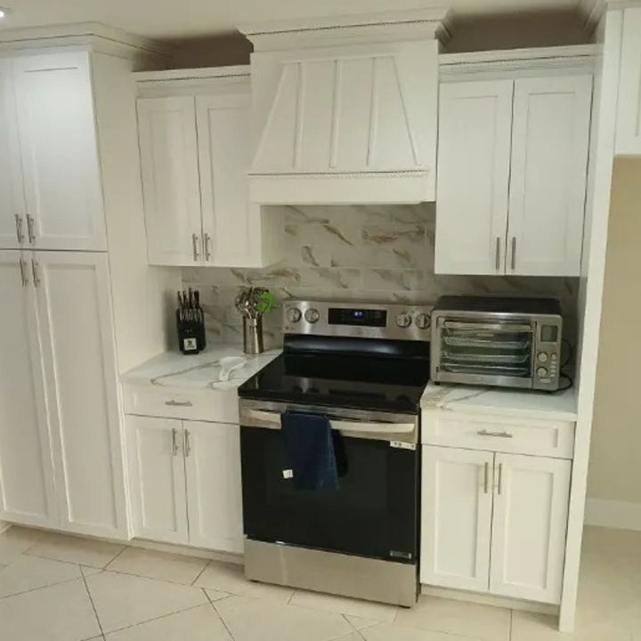 White kitchen with marble backsplash, black stove, and built-in cabinets.