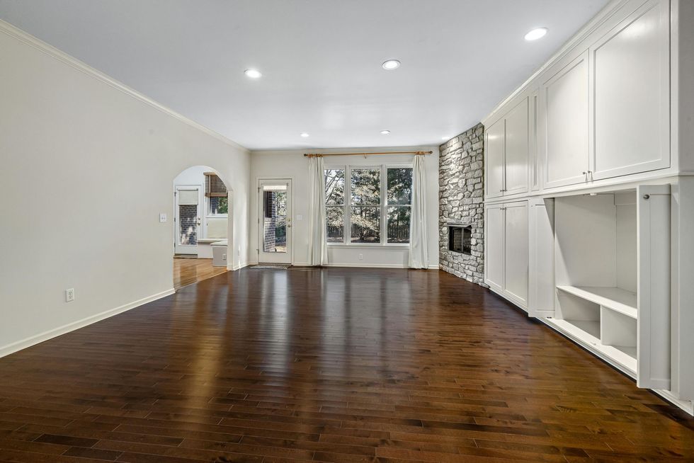 Empty modern living room with dark hardwood floors, white walls, recessed lights, and large windows.