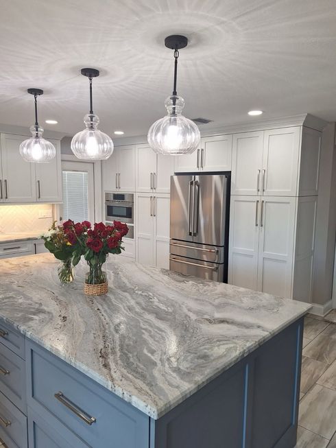 Modern kitchen with blue island, marble countertop, white cabinets, stainless fridge, and pendant lights