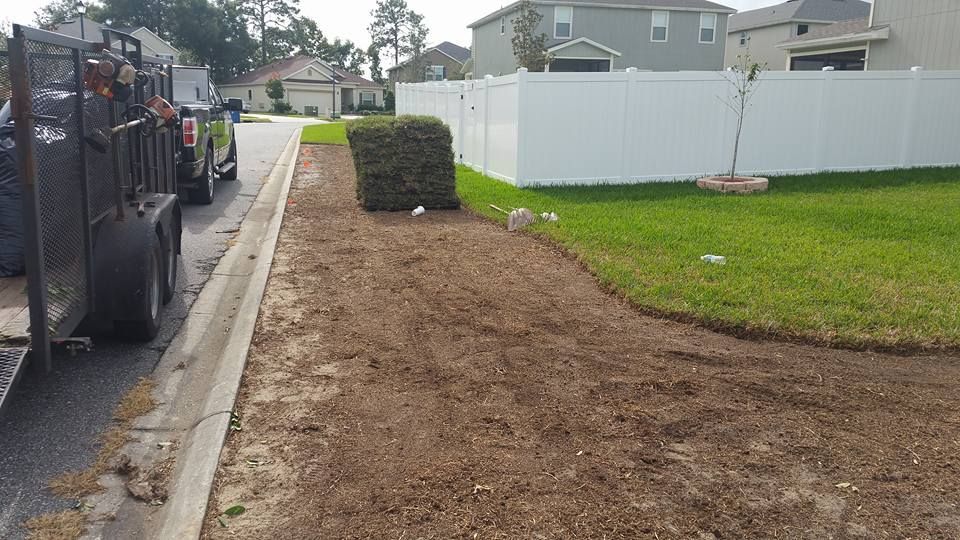 A lawn maintenance crew parked on a residential street next to a freshly cleared dirt strip and a green yard.