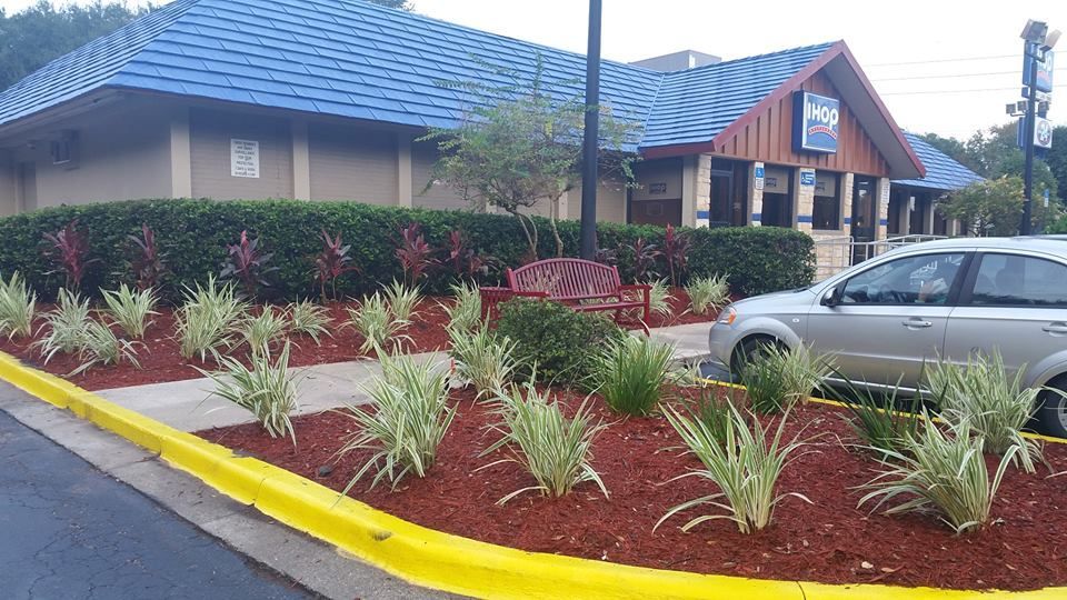 A restaurant with a blue shingled roof, a mulched garden with ornamental grasses, and a silver car parked on the side.