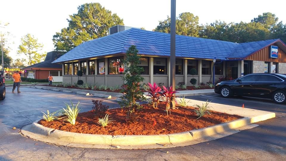 A restaurant building with a blue shingled roof, a parking lot, and a small landscaped garden in the foreground.