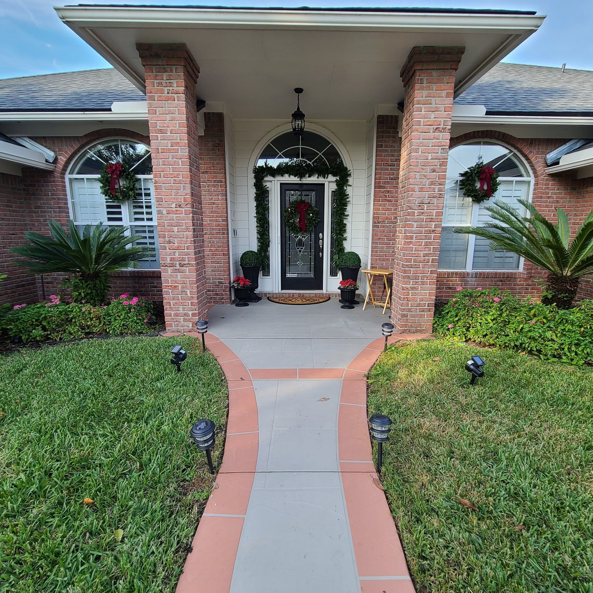 Front porch with brick columns, wreaths, and a curved walkway leading to a decorated front door.