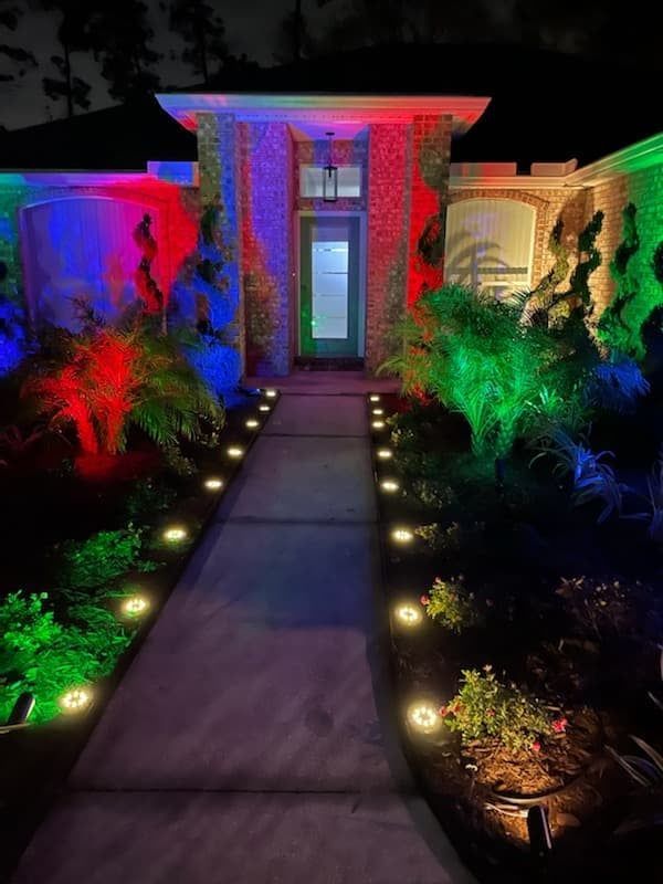 Colorfully lit walkway leading to a front door at night, with red, blue, and green garden lighting