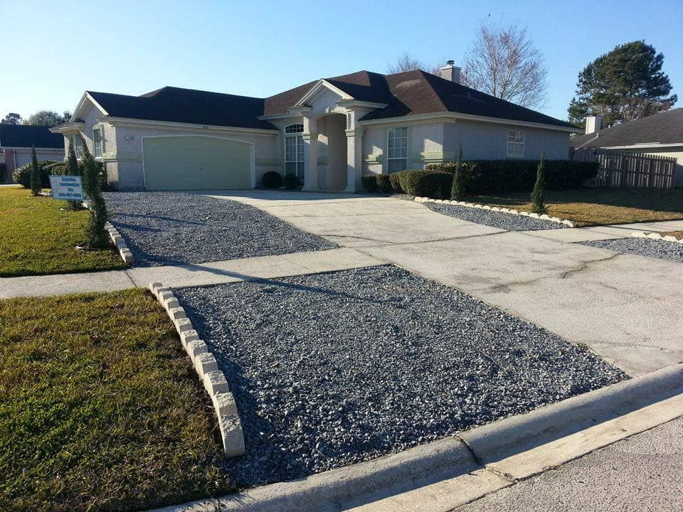 A single-story suburban house with a concrete driveway featuring decorative gray gravel sections and stone edging.