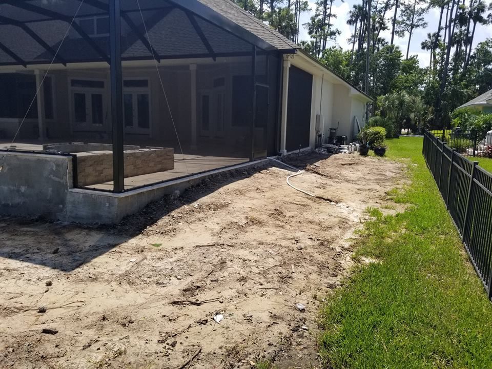 Exterior view of a home with a screened-in patio and a concrete foundation beside a dirt yard and a black metal fence.