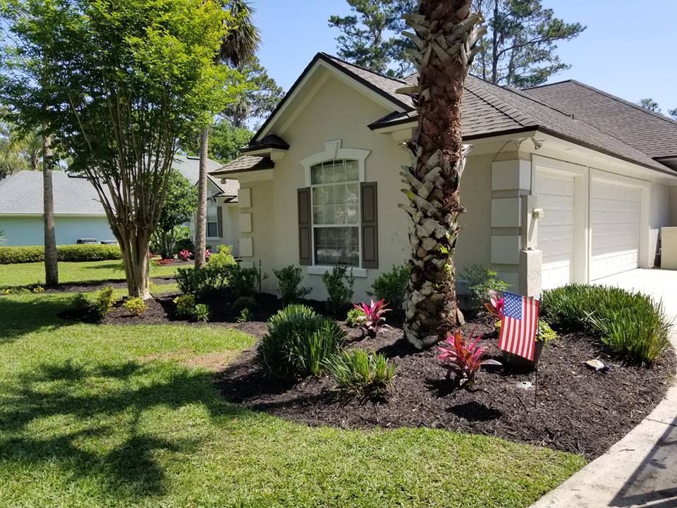 Single-story house with landscaped front yard, palm tree, and small American flag by the walkway