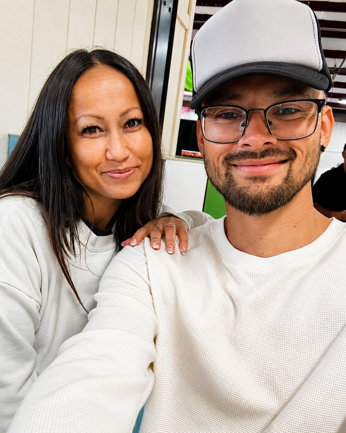 Two people smiling in white sweaters, posing closely indoors.